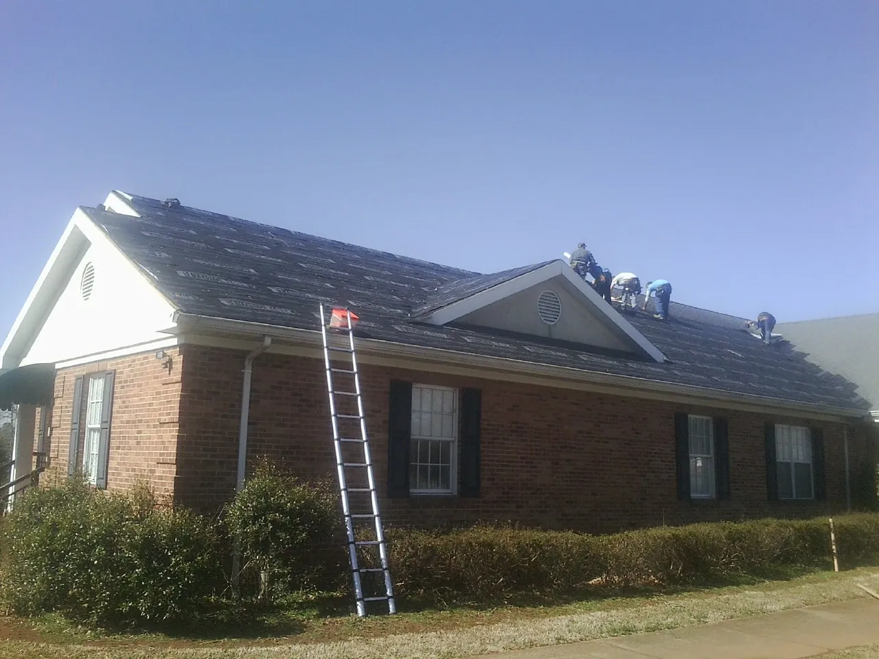 Crew tearing shingles off a brick ranch roof with a ladder set — Metal Roof Repair work by our crew in Owings Mills