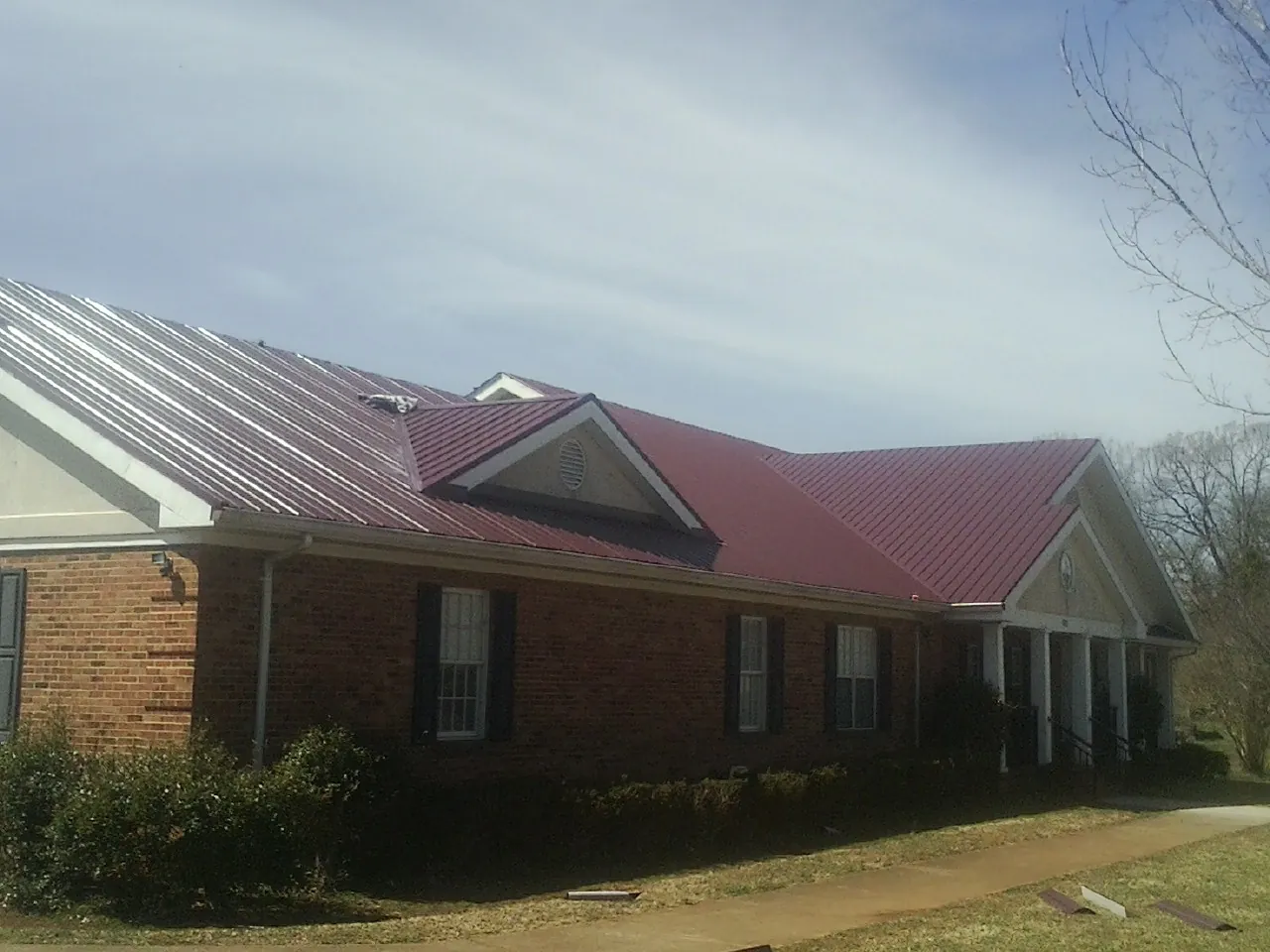 Red metal roof with gabled entries on a long brick building, from a Hail Damage Roof Repair job in Owings Mills