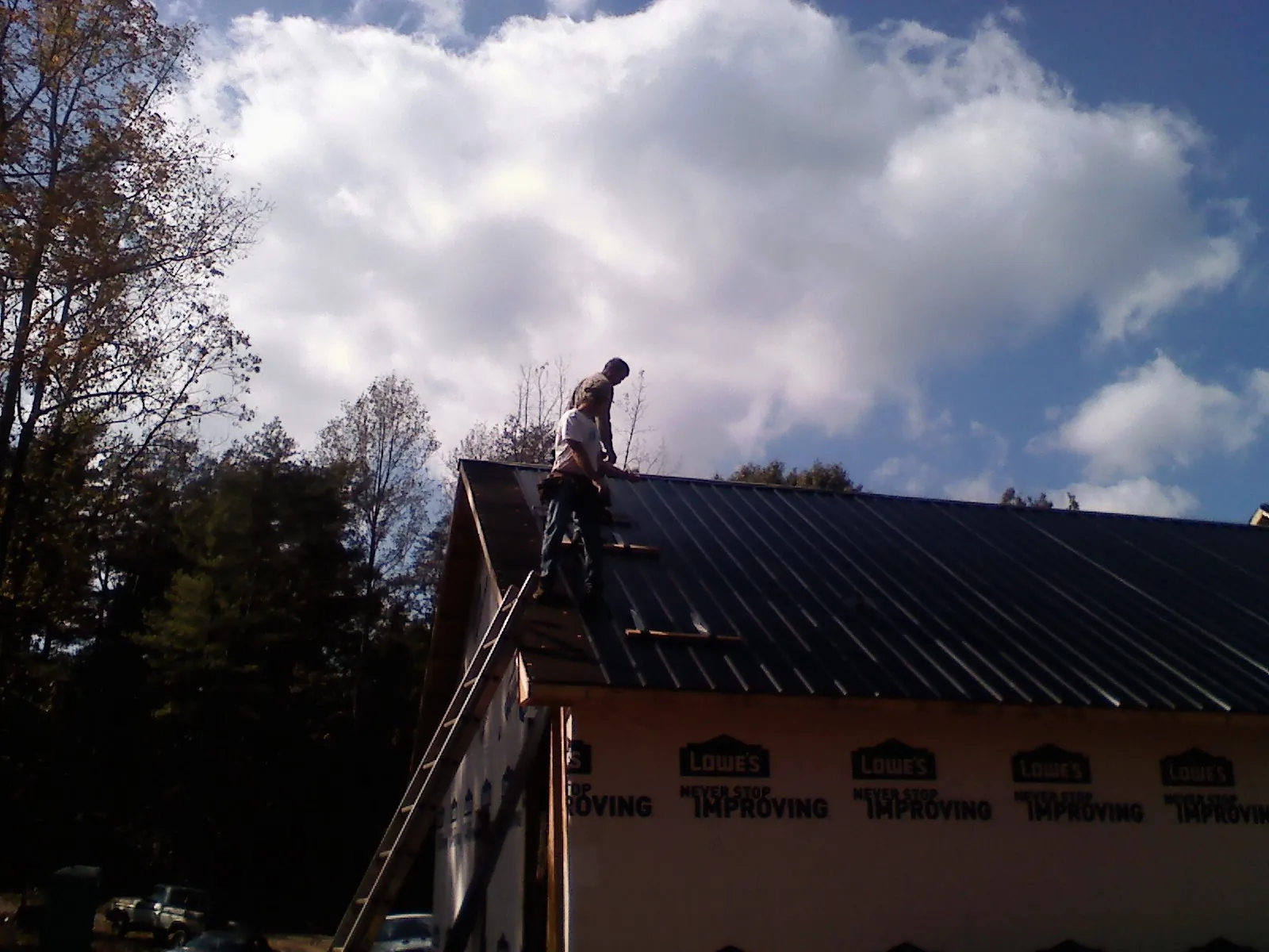Roofer fastening dark metal panels high against a cloudy sky, from a Roof Inspection job in Owings Mills