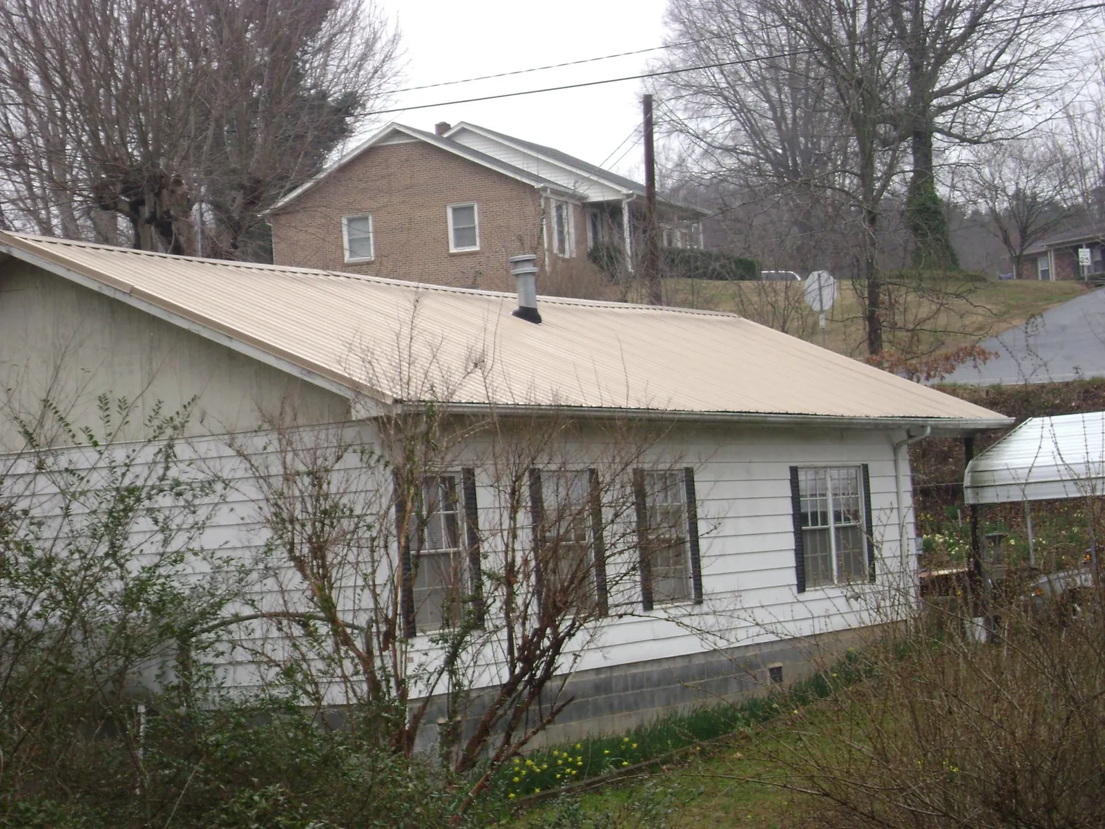 Tan metal roof on a white sided house set into a hillside — Commercial Roofing by Roofing Brothers in Owings Mills